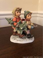 Front view of the Berta Hummel figurine showing two children carrying a Christmas tree with detailed clothing and expressions.