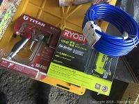 Overview of Titan spray gun in packaging, Ryobi brad nailer box, and blue hose in yellow bin