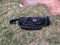 Black Acuity golf bag with shoulder strap resting on grass next to some flagstone and dirt.