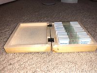 Opened wooden box with multiple prepared microscope slides inside, each slide labeled and stored upright in foam slots.
