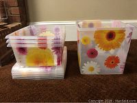 Four floral-themed plastic storage containers from The Container Store stacked and displayed to show size difference and floral designs.