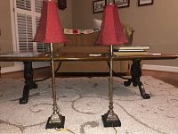 Two skinny buffet lamps with red shades side by side on carpet in front of a wood coffee table.
