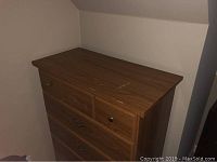 Brown wooden dresser against a neutral wall showing top surface scratches and front five drawers with metal drawer pulls.