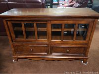 Entertainment center table with glass paneled doors and drawers, shown from the front.
