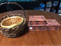 Two soft floral patterned jewelry boxes stacked next to two woven baskets on wooden table.