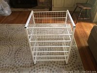 White metal Elfa closet organizer with three sliding wire mesh drawers displayed on a rug in a room, showing front and top view