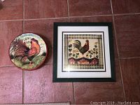 Photo shows a round decorative plate with a rooster illustration and a square framed print also featuring a rooster with a checked border and heart/flower motifs.
