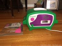 Easy Bake Oven with box and baking tools displayed on floor. Oven is green, purple, and white with Girl Scout logo.
