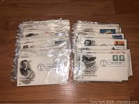 Two stacks of over 50 First Day of Issue envelopes from 1985, each in protective plastic covers, displaying various stamps and postmarks with historical and thematic prints.
