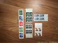 Photo showing multiple blocks and strips of collectible vintage stamps including Lincoln, JFK, Churchill, Disney, and UNESCO themes laid out on wooden floor.