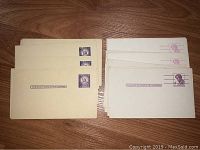 Set of two stacks of unused vintage pre-stamped postcards, one with 4 cent Lincoln stamps in blue and the other with 3 cent Statue of Liberty stamps in purple.