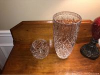 Image showing a small Waterford crystal bowl with starburst pattern beside a tall Mikasa crystal vase, both placed on a wooden surface.
