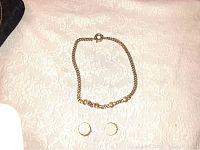 Top view photo of the vintage gold-plated Versace necklace and two gold-plated rings arranged on a light patterned fabric.