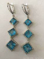 Front view of earrings showing three large square blue stones in sterling silver setting with lever-back closures.