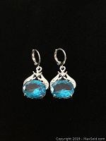 Pair of silver tone earrings with large blue oval faceted stones on black background.