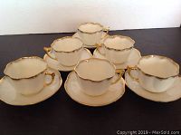Six white antique porcelain tea cups with matching saucers, all with scalloped edges and gold trim on rims and handles.