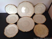 Top-down view of all eight luncheon plates arranged in a clustered layout showing gold trim edges and embossed patterns.