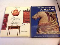 Two books side by side on a white surface. Left is 'The Anatomy of Antiques' and right is 'The World Guide to Antiquities'.