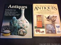 Two hardcover antiques reference books on a flat surface. The first book titled 'Antiques' with images of antiques on cover; the second titled 'The Collector's Encyclopedia Antiques' by Phebe Phillips with images of antique furniture and items on cover.