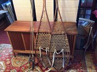 Overall view of the pair of wooden snowshoes with woven webbing leaning against a wooden cabinet.