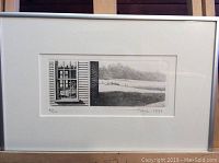 Full framed etching artwork under glass showing a rural window and landscape scene.