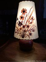 Dornbusch lamp illuminated showing floral pattern shade sitting on round pottery base with scalloped top trim.