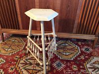Front angled view of wooden plant stand showing pentagonal top and spindle supports.