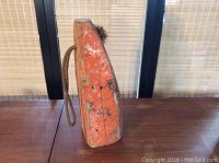 Side view of the orange wooden buoy showing paint wear and attached rope.