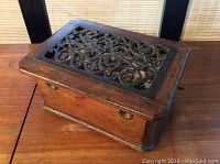 Front view of antique foot warmer with wooden box, ornate metal grill on top, and side handles