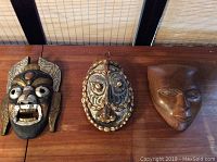 Three small tribal style masks displayed on a wooden surface