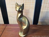 Front and side view of a brass cat figurine showing smooth and shiny surface with clean lines and minimalist, stylized design.