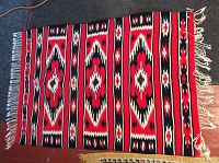Floor covering laid flat showing full front Aztec design with red, black, white, and beige colors and fringe tassels on edges