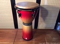 Full view of the djembe drum showing red-yellow gradient body and Apple logo