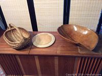 View of all three items on a wooden surface: woven apple basket, wooden round bread board, and large wooden salad bowl.