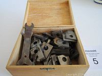 Open wooden box filled with assorted metal bits and a double-ended wrench inside.