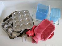 Photo showing 3 metal muffin tins, clear glass Pyrex tart pan, blue plastic containers, and 2 red rubber hot water bottles.