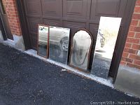 Four assorted wall mirrors placed outside against a garage door showing size and frame styles