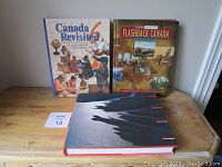 Photo showing three hardcover Canadiana coffee table books standing and lying on a wooden table.