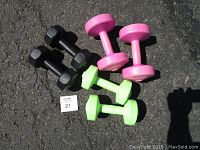 Three pairs of dumbbells on pavement, showing different colors and sizes