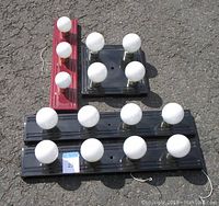 Four ceramic flush mount lighting fixtures shown from above, arranged on pavement. Includes one red rectangular base with 5 white bulbs, one black rectangular base with 11 white bulbs, and one smaller black square base with 4 bulbs.