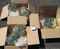 Top view showing two open cardboard boxes containing four smaller polygonal flush mount ceiling light fixtures with brass or gold-tone frames and clear glass panels, partially wrapped in bubble wrap.