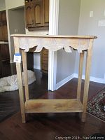 Front left angled view showing rustic whitewashed finish and carved floral detailing under the tabletop along with lower shelf.