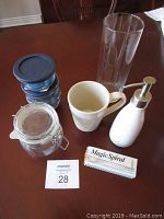Photo showing each item in the lot arranged on wooden table: glass vase, storage bowls, mug, glass jar, soap dispenser, spiral cutter.
