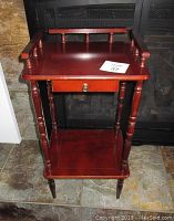 Small red wooden side table with one drawer and turned legs in front of a dark background