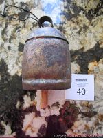 Metal rustic bell with handle on top, showing weathered and rusty surface, positioned on marble counter.