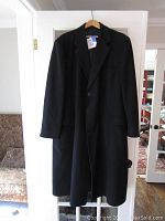 Full front view of the long black wool coat hanging on a wooden hanger, showing overall condition and style.
