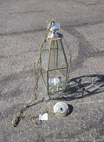 Full view of the 32-inch glass chandelier laid on asphalt. Shows metal chain, wiring, and glass panels set in brass frame with missing glass door panel.