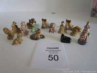 Overall view of 15 Wade Red Rose porcelain figures arranged on white surface, showing different animals and human characters, mostly brown and cream colored.