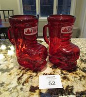 Pair of red glass beer boots shaped like hockey skates with Molson Canadian labels on granite countertop with auction lot card '52'.