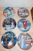 Six collector plates displayed on a table, five Disney themed and one bears plate.